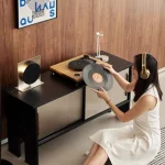 Woman placing a vinyl record on a turntable next to a vinyl record storage cabinet